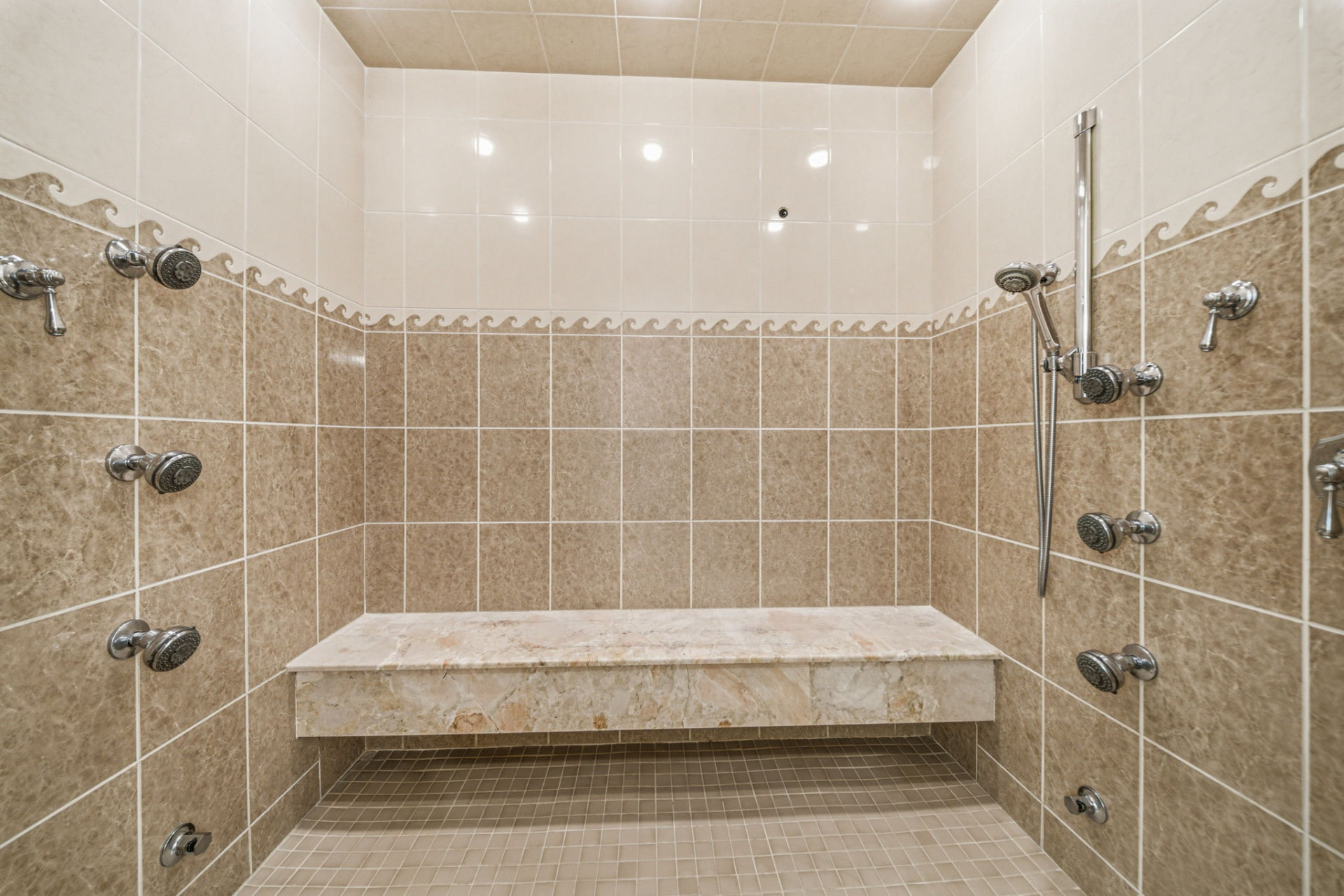 Oversized tiled steam shower with multiple body sprays and stone bench