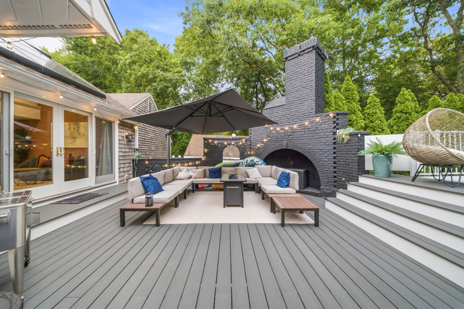 Wide deck view with sectional, fire table and black brick fireplace